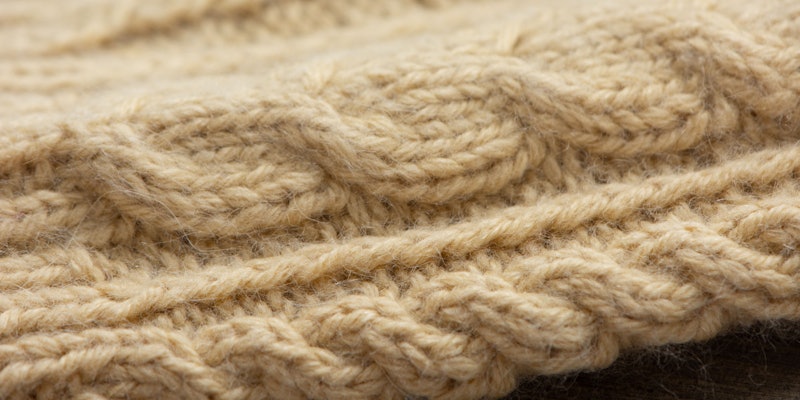 A closeup image of a mustard yellow cabled sleeve.