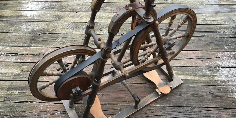 An antique spinning wheel with two drive wheels that are connected by a band of leather.