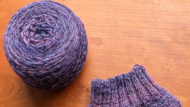 A ball of yarn and a cuff of a sock on a wooden background.