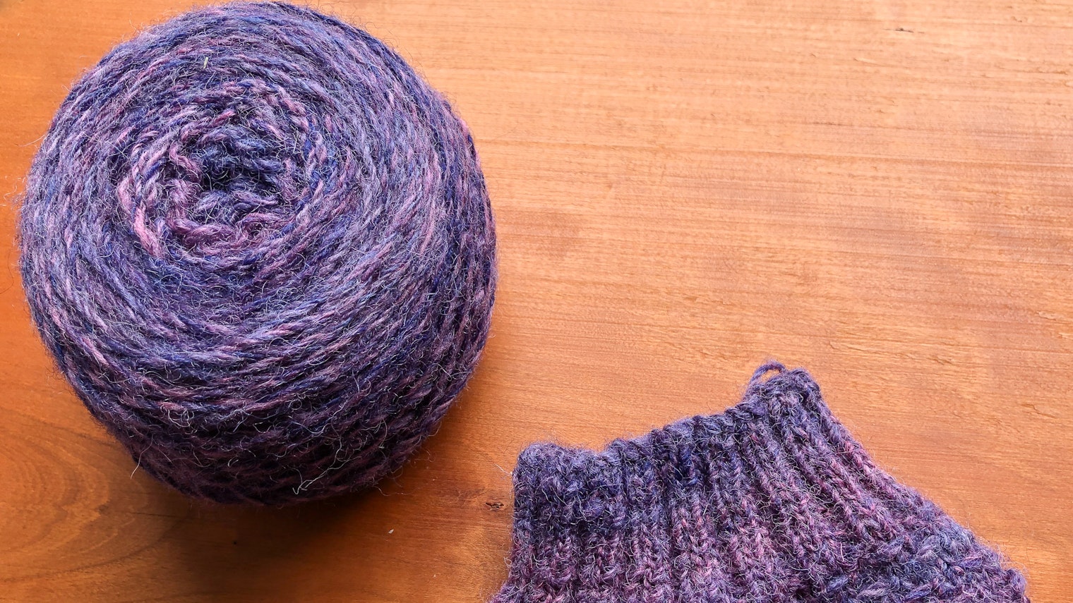 A ball of yarn and a cuff of a sock on a wooden background.