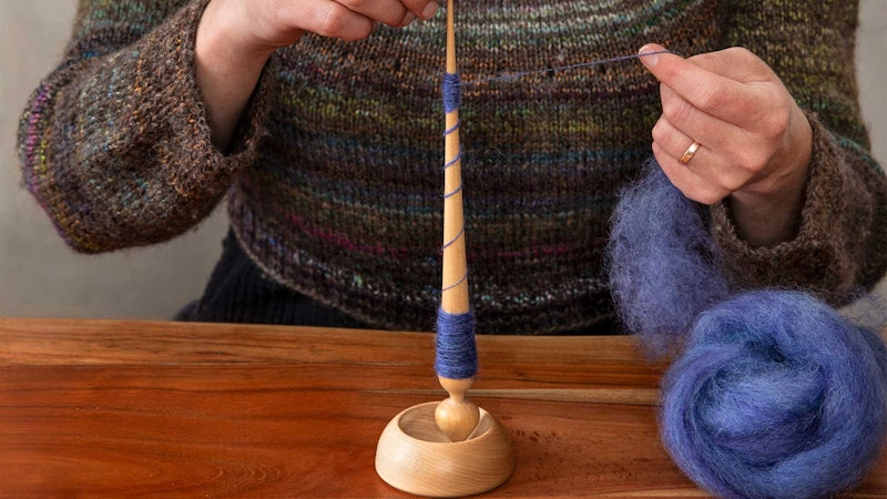 Spinning on a supported spindle. Blue fiber on a table.