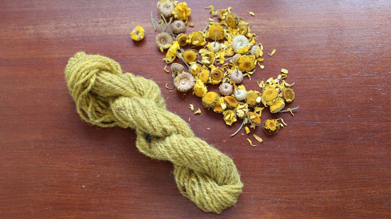 A yellow skein of yarn and dried yellow flowers on a wooden surface.