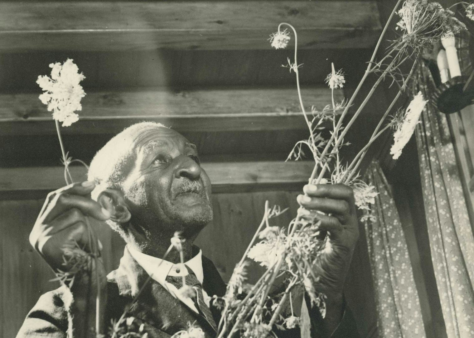 A black-and-white photograph of a man wearing a suit and holding wildflowers.