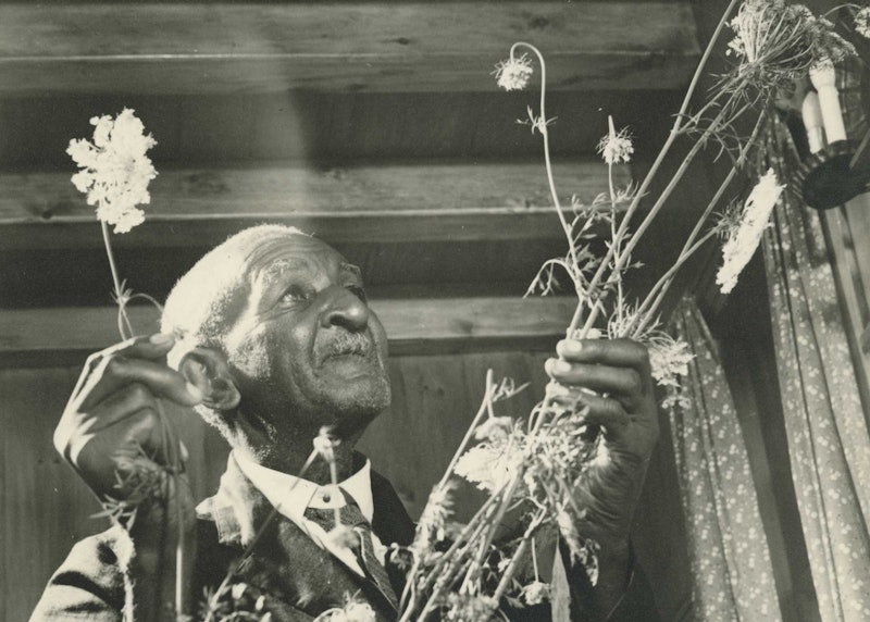 A black-and-white photograph of a man wearing a suit and holding wildflowers.