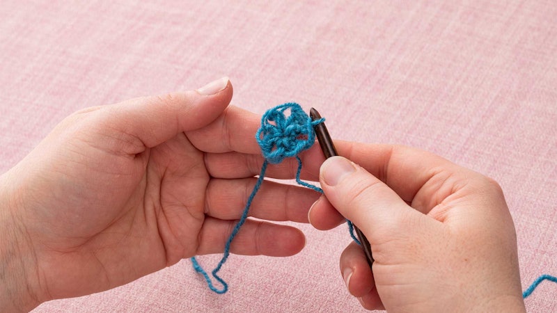 Hands holding a small crocheted circle and a wooden crochet hook