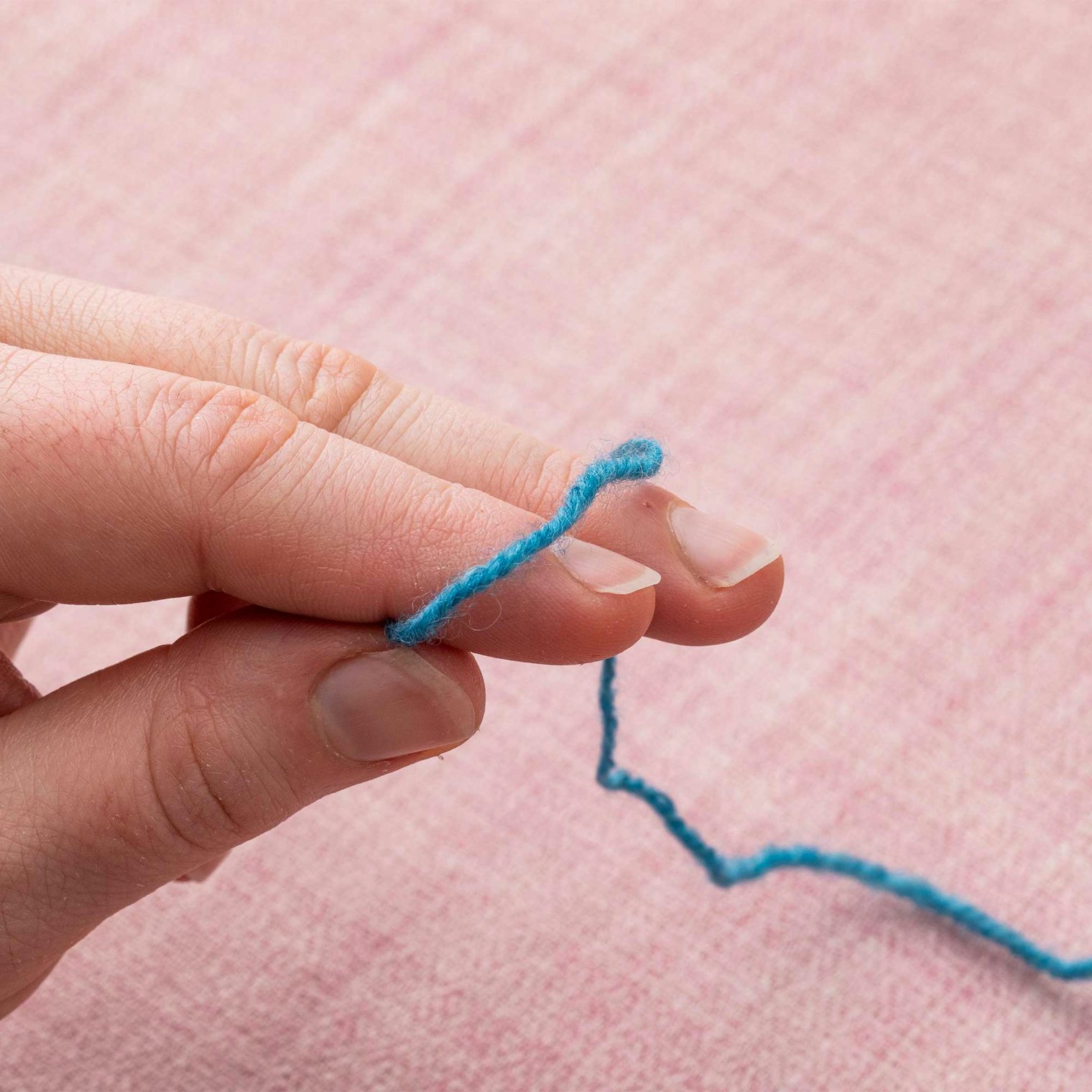 Hold the end of your yarn between thumb and forefinger. Let the long end of the tail drape over your middle finger and away from you.