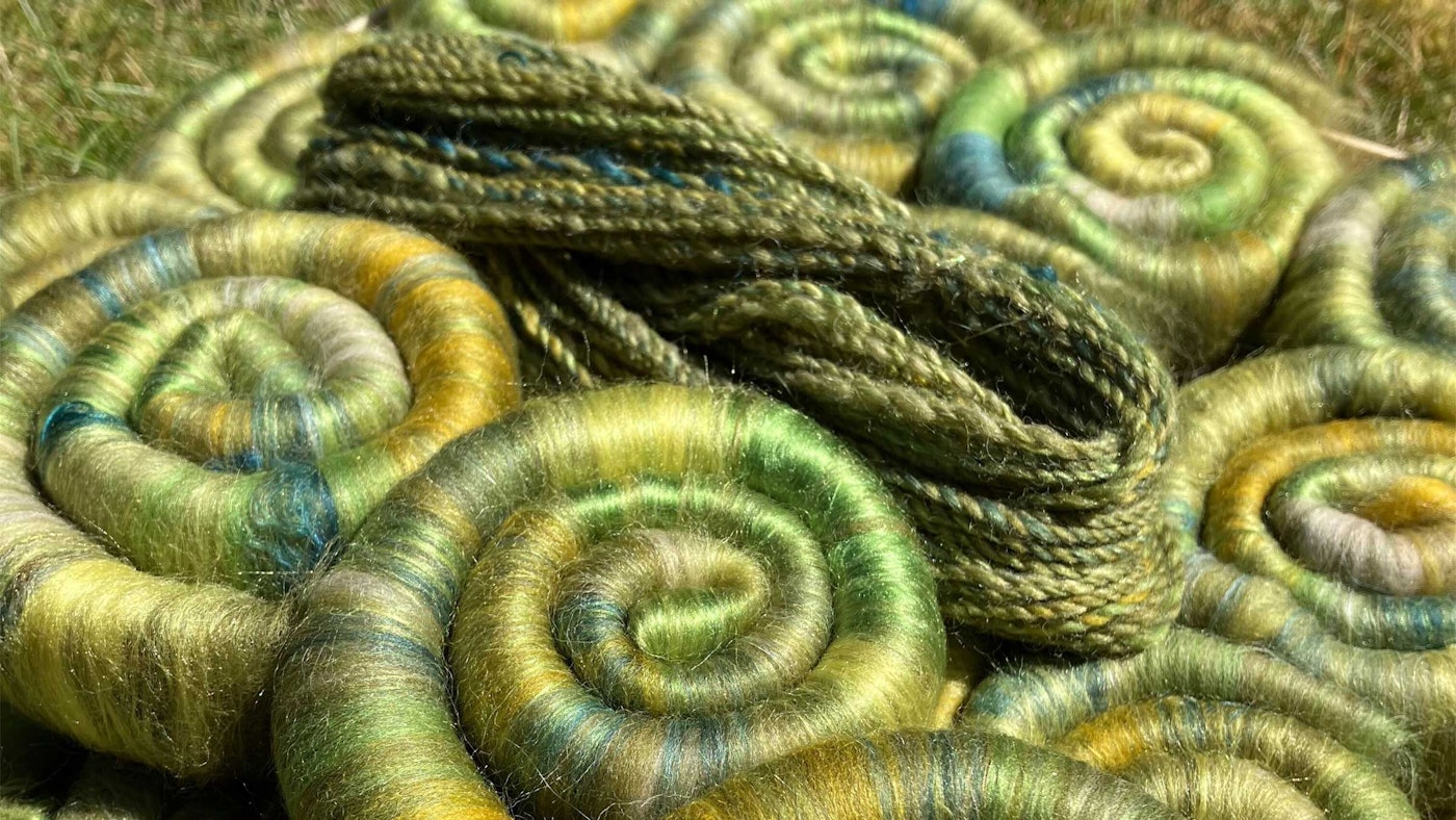 olive green rolags and handspun yarn on a grassy surface