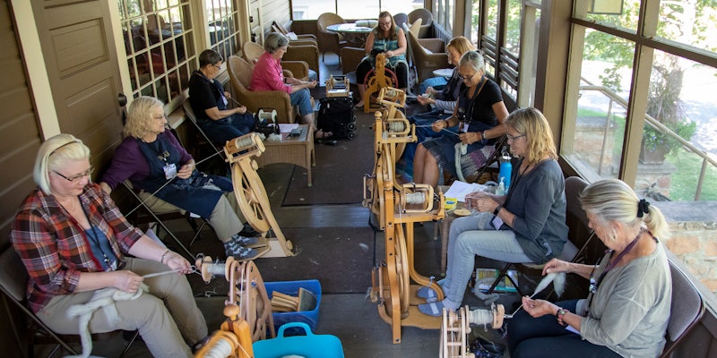 A group of spinners on a porch with their spinning wheels.