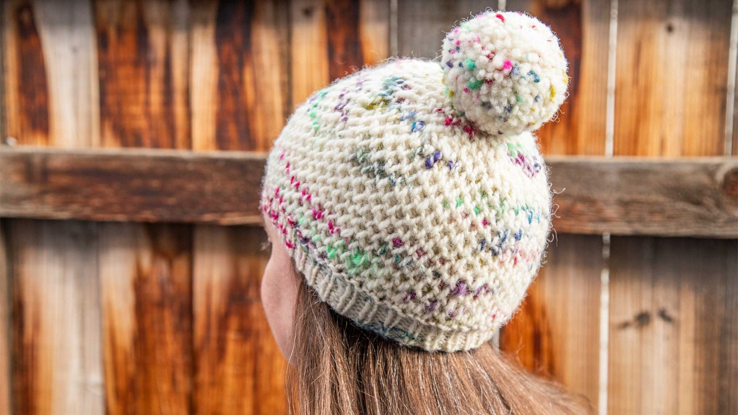 The back of a person's head. The person is wearing a speckled beanie with a pom pom.
