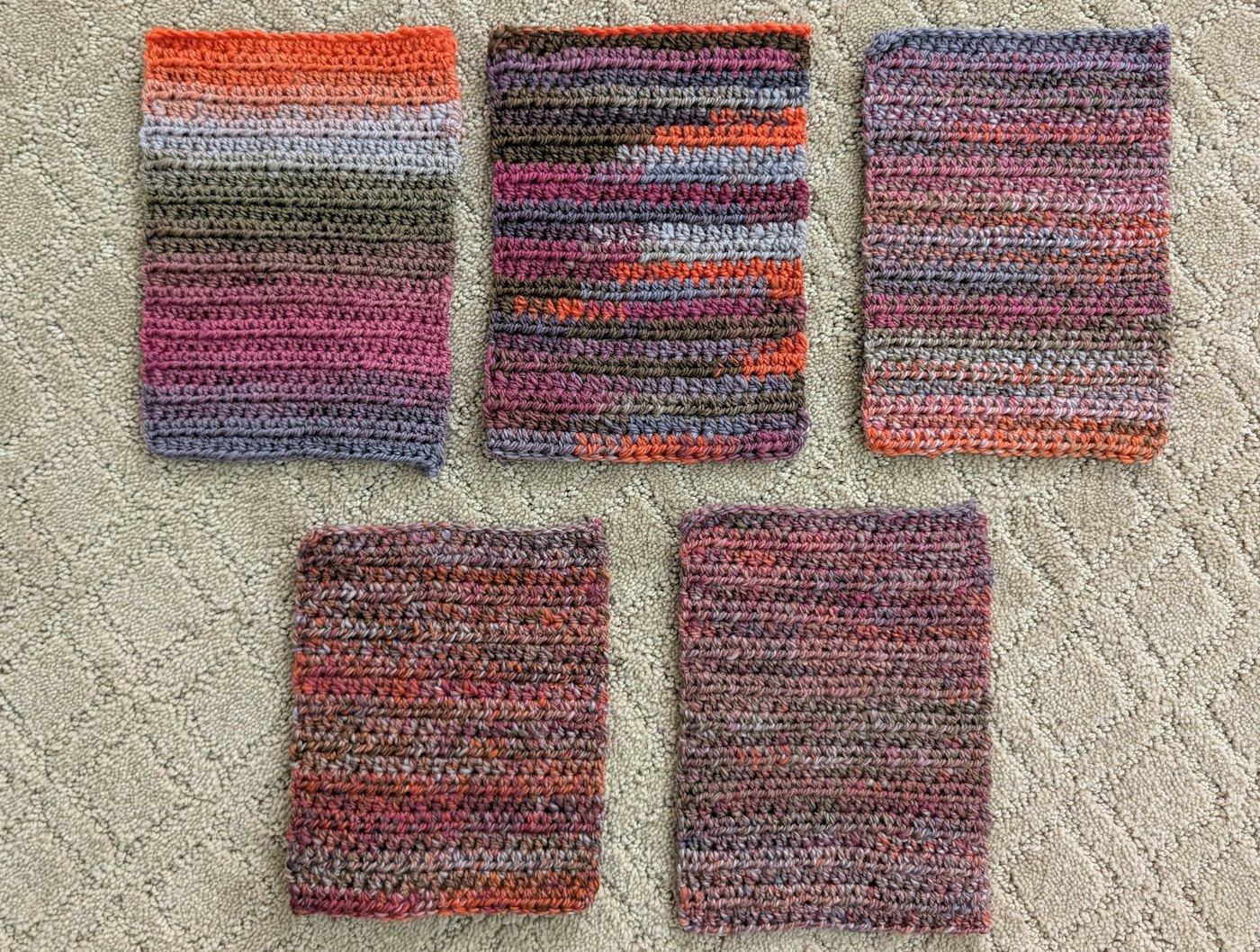 5 crocheted rectangles in similar colors shown on a carpeted floor.
