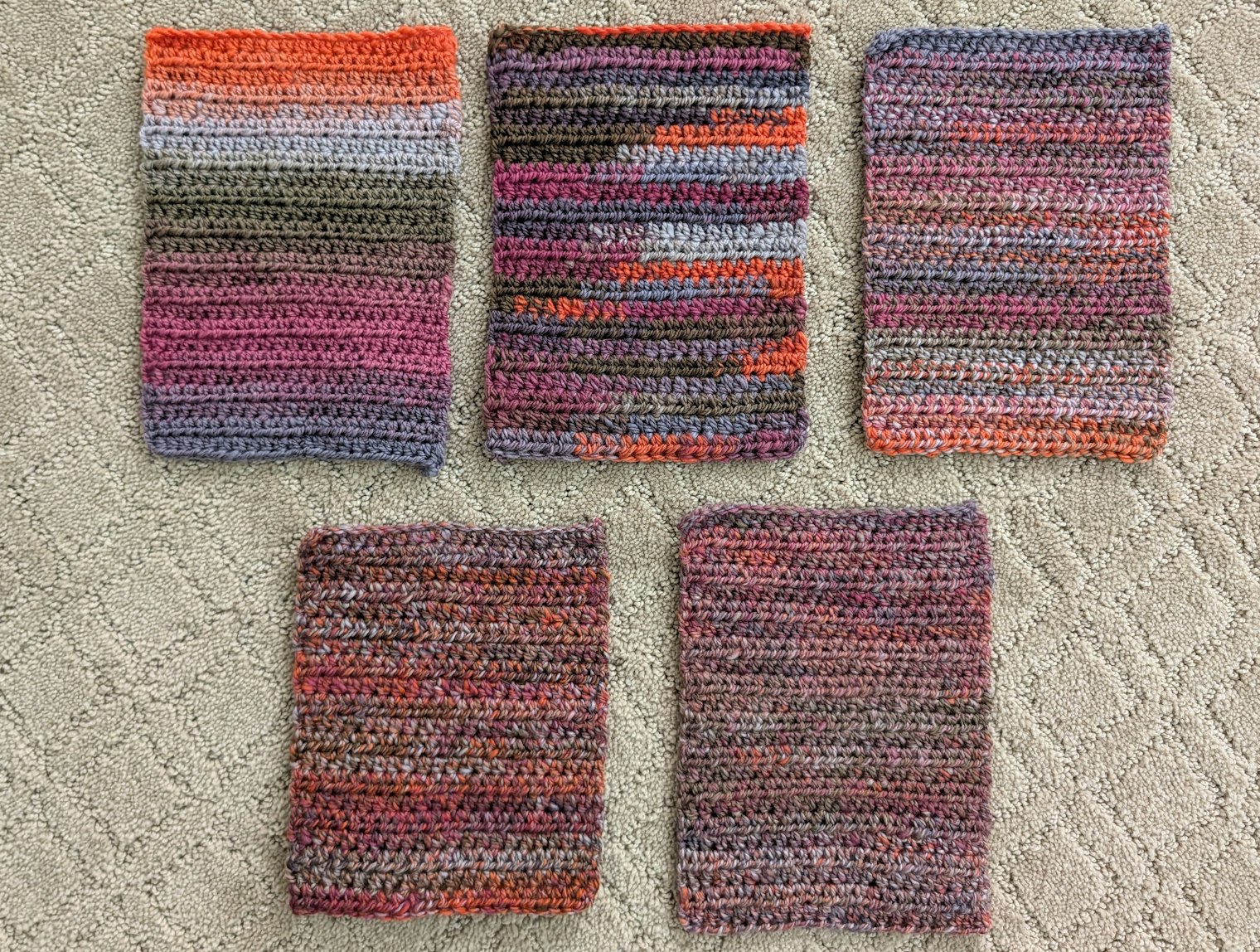 5 crocheted rectangles in similar colors shown on a carpeted floor.