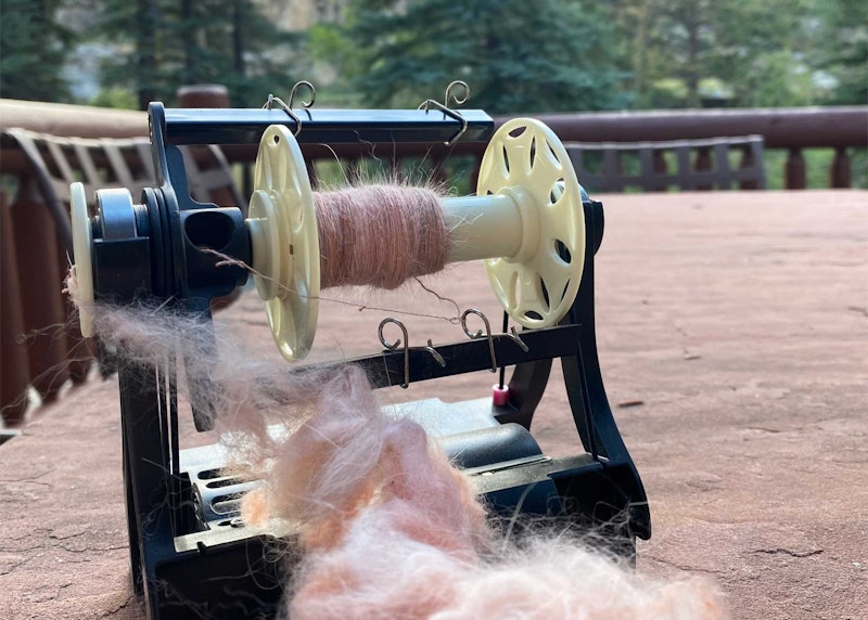an electric spinning wheel with fluffy pink yarn and fiber.