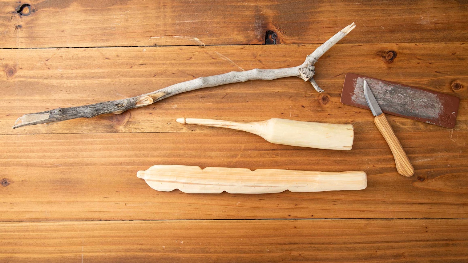 A tree branch, a knife, and sharpening strop shown alongside a hand-whittled spindle and distaff.
