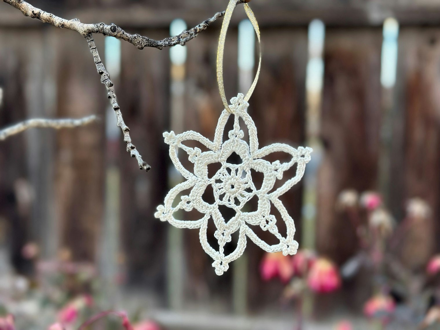 A crochet snowflake ornament is hanging from a branch in a tree.