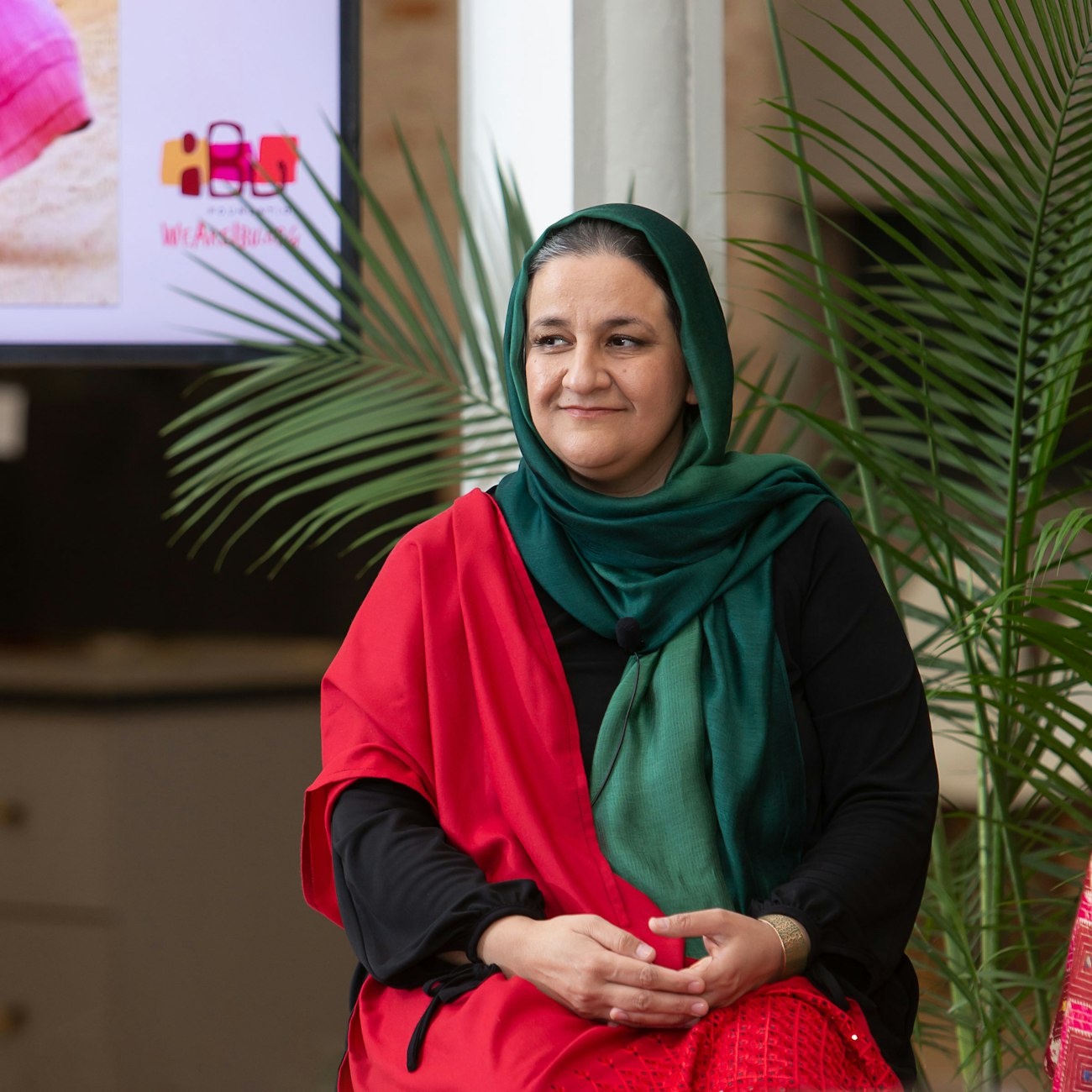 Seated woman in black dress, hair covered with green shawl, red shawl over right shoulder