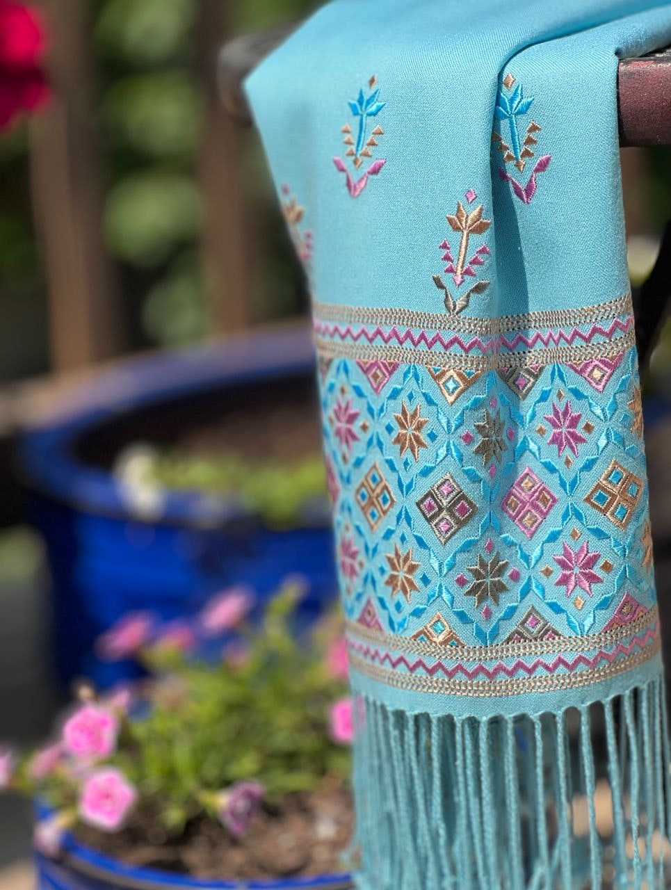 Blue embroidered shawl against a background of flowering plants in pots