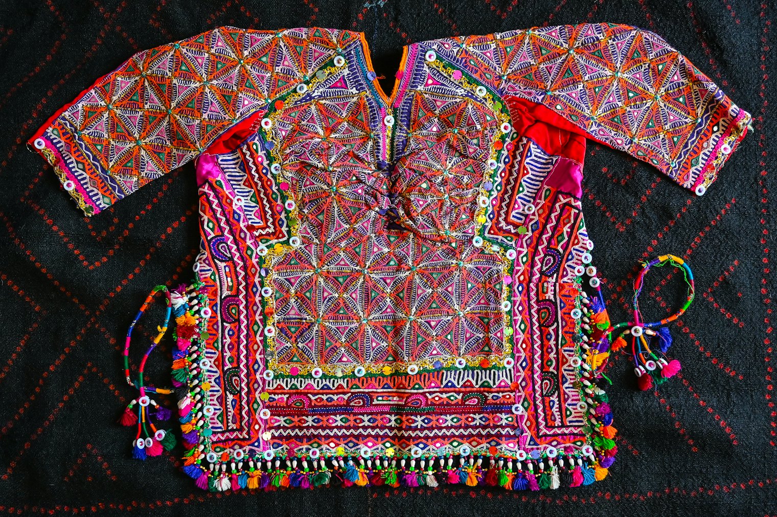 Kanchali, festival blouse, Kachhi Rabari, circa 2000. In the 1990s, to save time and effort while embroidering, Kachhi Rabari women began to use machine zigzag stitching to outline motifs and filled in mirrors and detailing by hand. In this early example of the innovation, the machine-stitched gold lines in the body of the blouse emulate the tight hand-embroidered chain stitch black outlines in the sides. The artisan filled the body with fine buttonhole and Romanian accent stitches and included bakhiya on the center front seam. Collection of the author.