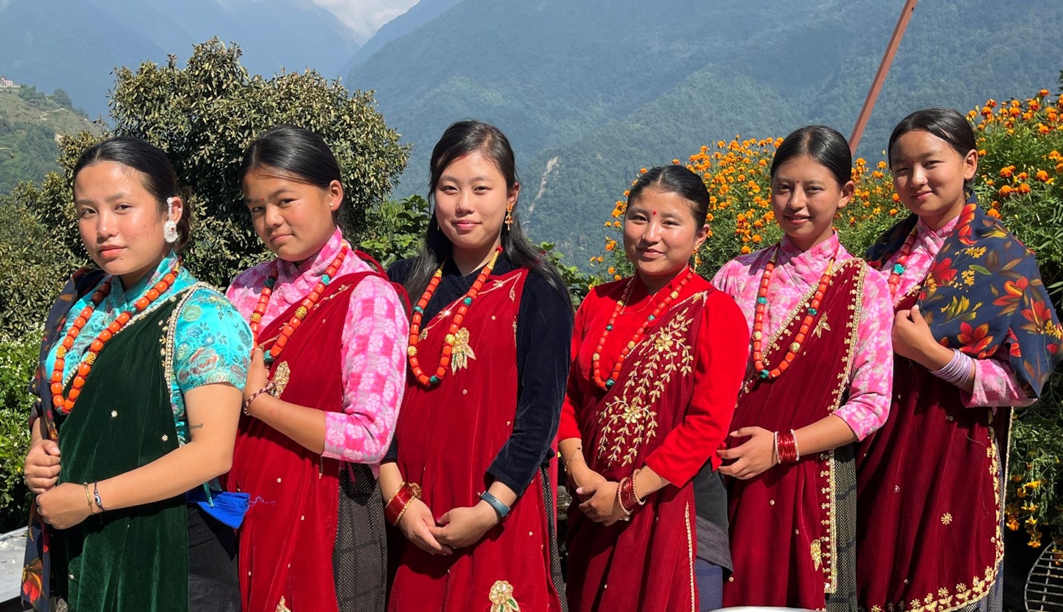 Young women show off their festival dress in Ghandruk. The black triangle of the tikish shows below the chaubandi cholo of the woman third from the right.