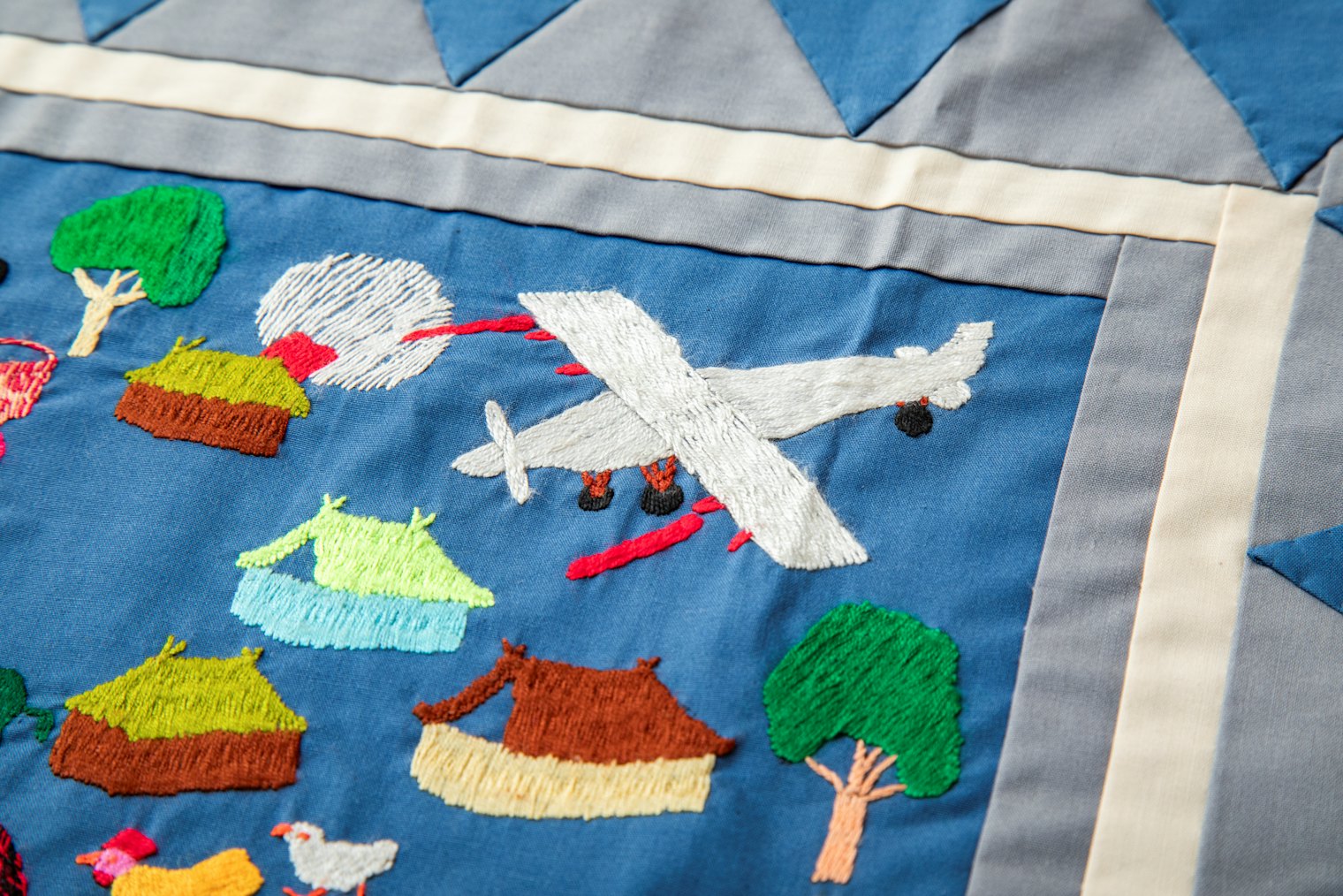 A Viet Cong fighter plane attacks a Hmong village, a detailed scene on Joyce's story cloth.
