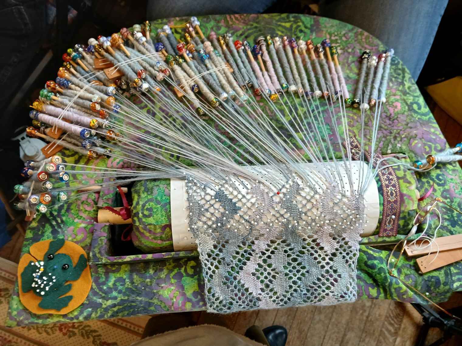 Contemporary lacemakers are not limited to trims and edgings or traditional fibers. Here a lace scarf is underway with larger fibers and larger handmade bobbins to hold long and heavier threads.