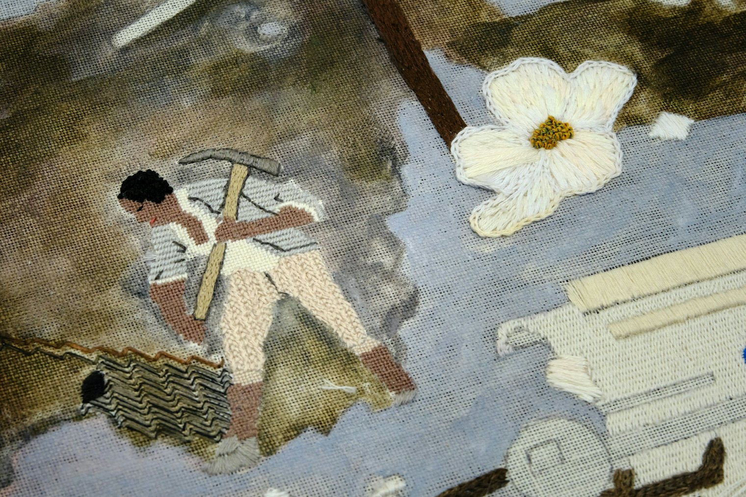 The man depicted here is a slave at work in the lead mine of Wythe County, Virginia. Catherine Theron brings him to life using DMC floss with petit point, long arm cross variation, diagonal satin stitch, and backstitch accents. His pick axe is worked in satin stitch, long and short, and backstitch. The mine background is painted by Catherine Jordan and the lead accents are stitched in diagonal wave stitch by Meghan Lochner. Virginia’s state flower, the dogwood, is stitched in colonial knots, reverse chain stitch, and long and short using overdyed Gentle Art threads.
