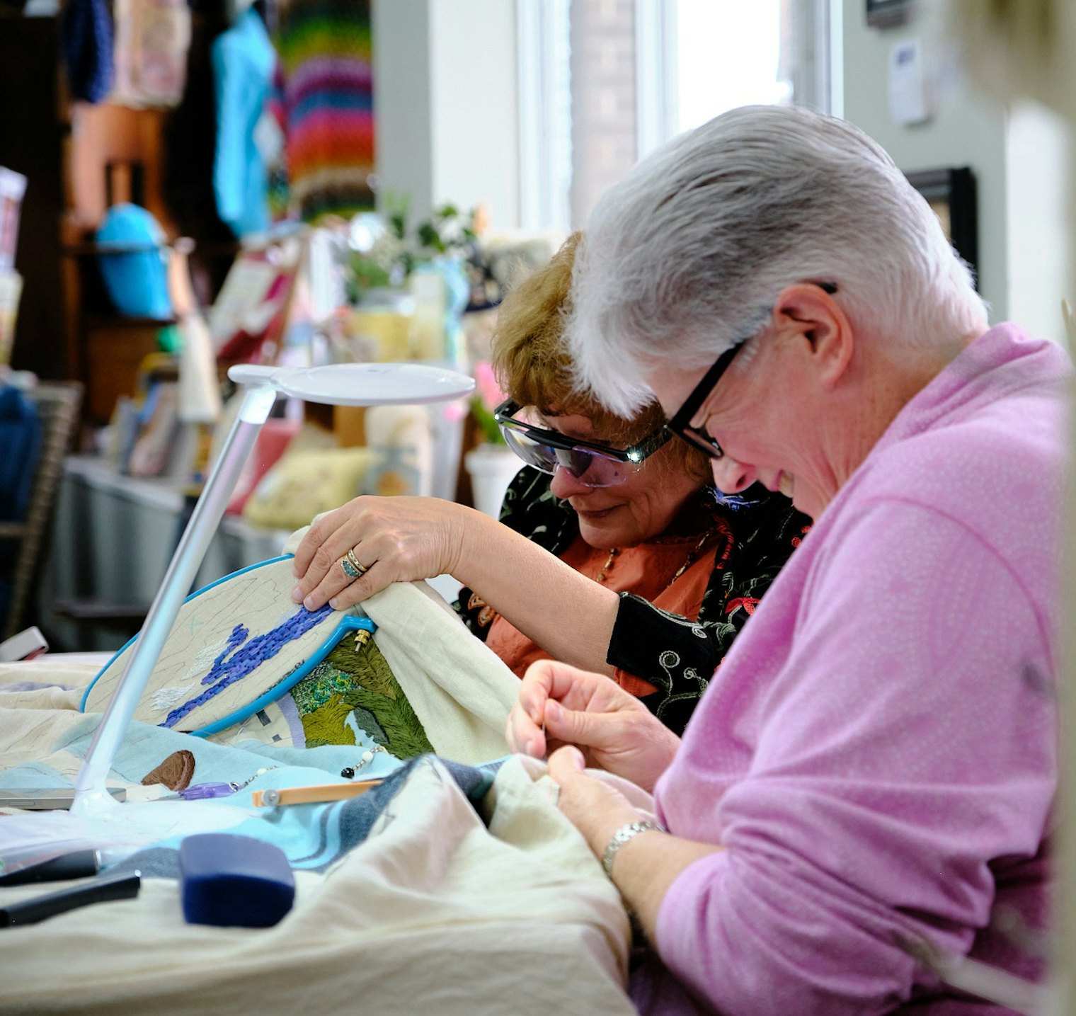 This photo was taken at Salty Yarns, a cross-stitch, needlepoint and yarn shop in Berlin MD. Moe Farrell is stitching on the sky, which contains herringbone, cross-stitch and darning stitch in DMC 3799, 315 and 169. Christine Giglio is stitching the water using the wave stitch, found on the Royal School of Needlework's StitchBank, with DMC 4240.