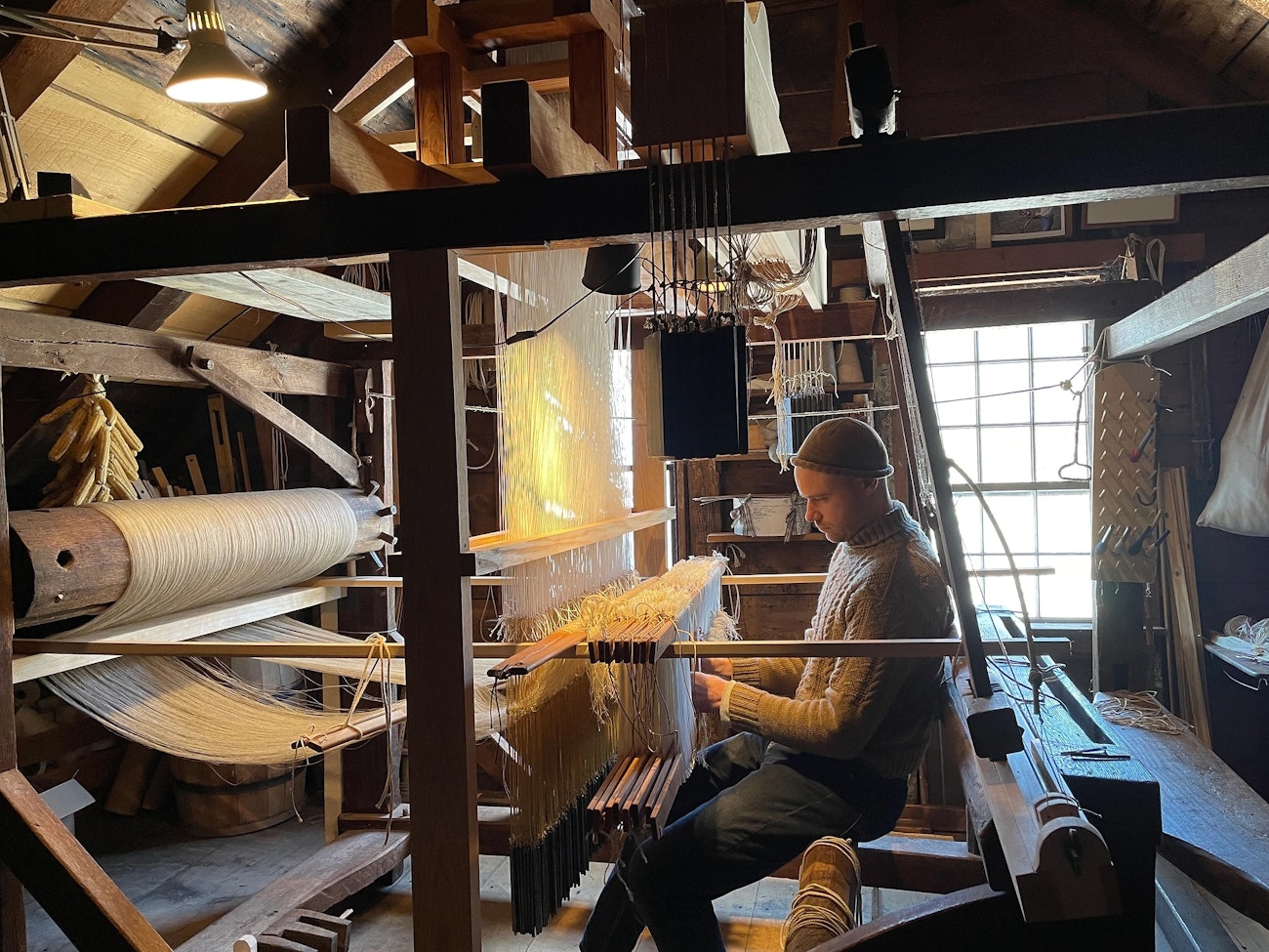 Man in wool beanie and gansey-style sweater dressing an antique loom