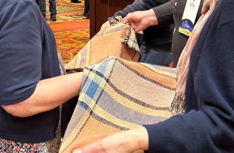 A handwoven shawl with people  holding it up to admire the fabric