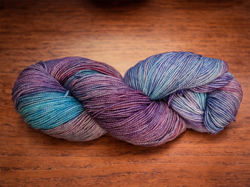 A blue and purple skein of yarn on a wood surface