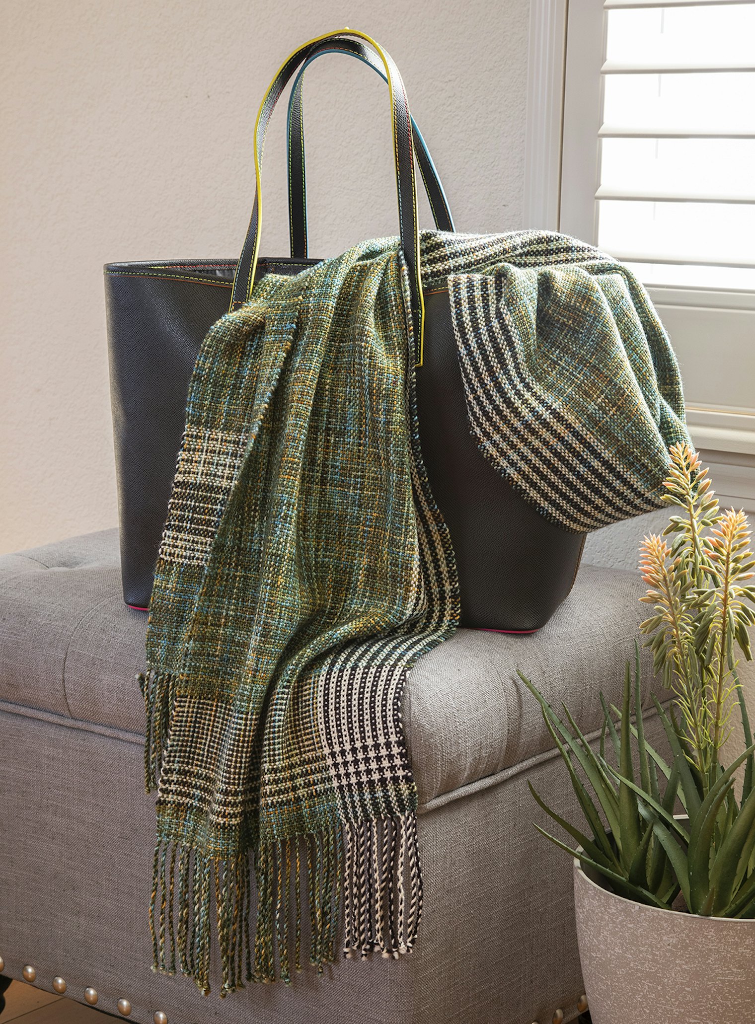 A scarf with white, black, and variegated green stripes draped on the side of a handbag.