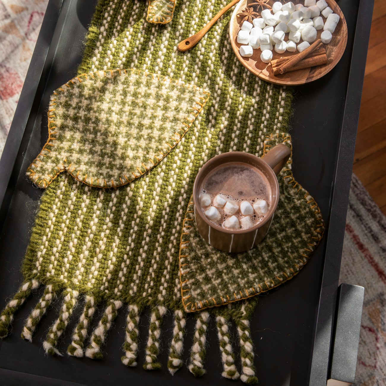 Green and white table runner  and felted leaf-shaped trivets sitting on a table with hot cocoa.