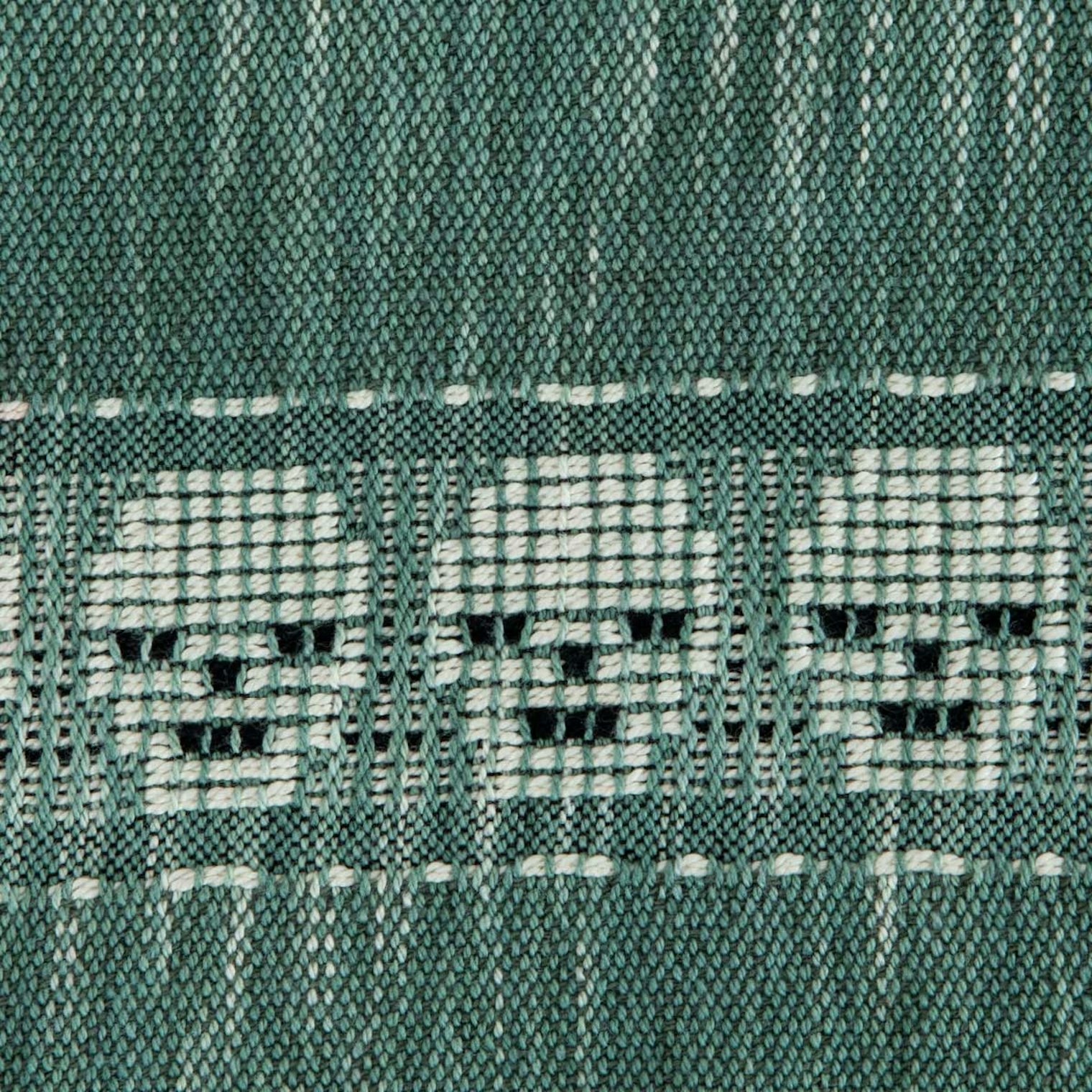 A variegated green textile with a series of white skulls.