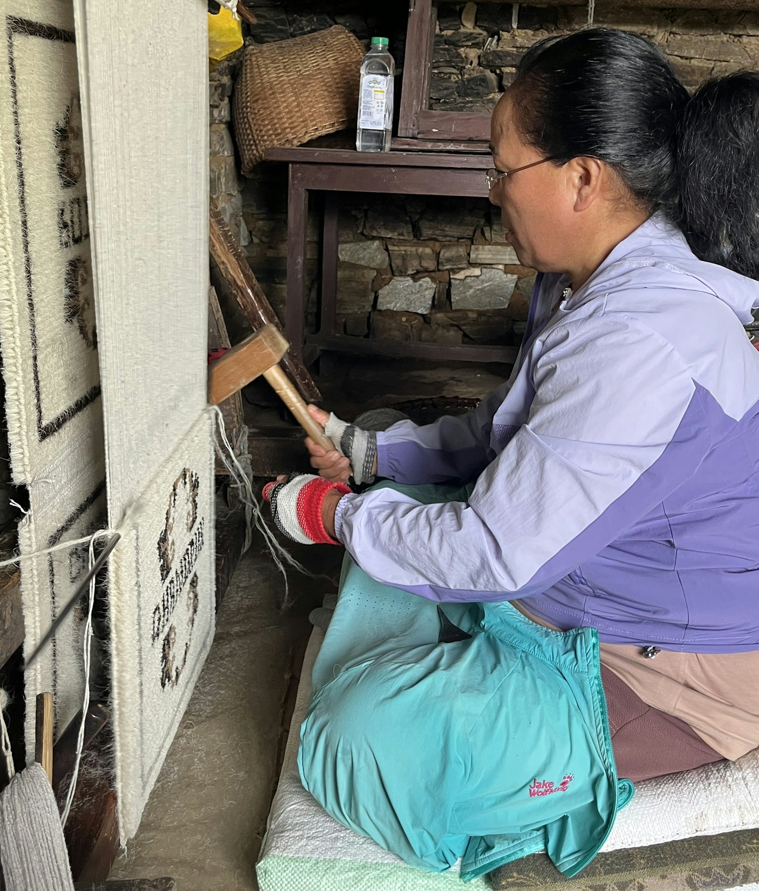 After tying a row of knots around the gauge rod, Purnima pounds it toward the fell line, beats the row in with a comb, and then cuts across the rod’s width to create pile.