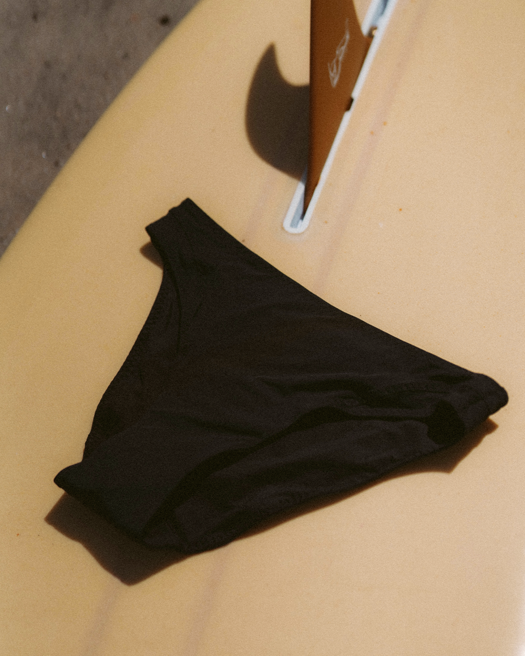 Black period-proof bikini bottom, lying on a surfboard.