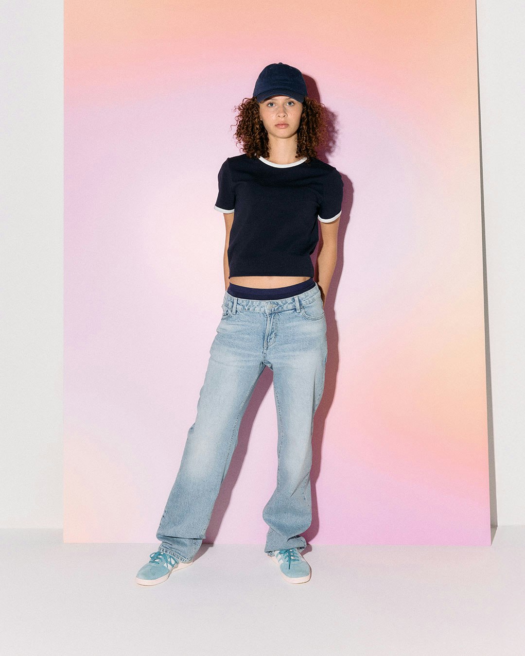 A person wearing a cropped top and light blue jeans against a pastel background