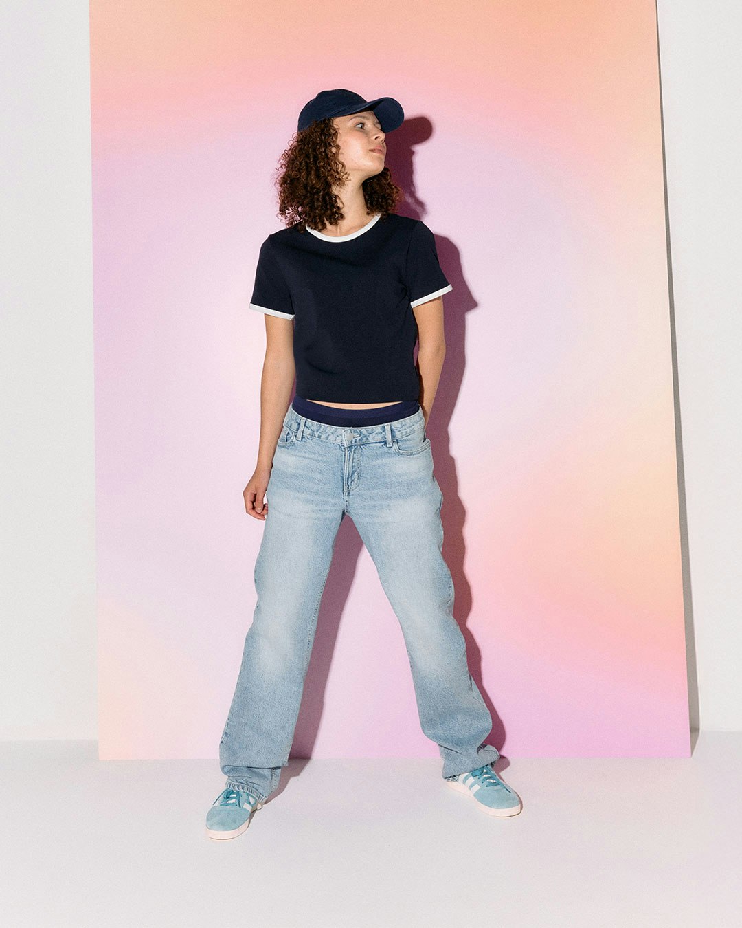 A person wearing a cropped top and light blue jeans against a pastel background