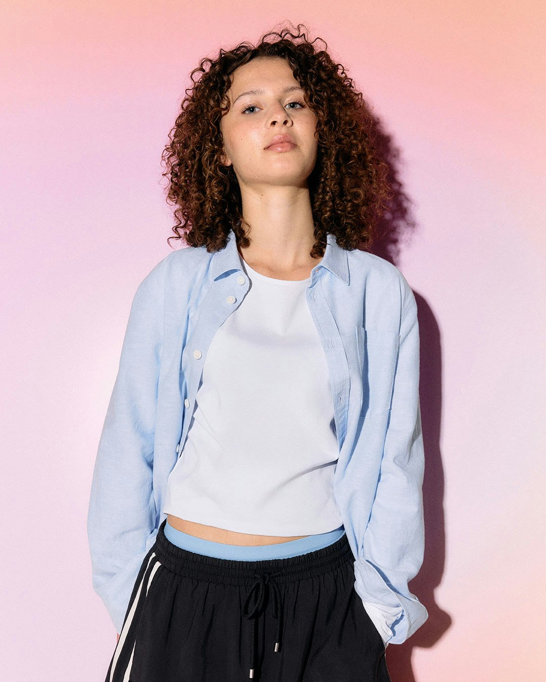 Person står foran en gradient bakgrunn i pastellfarger, iført skjorte og shorts.