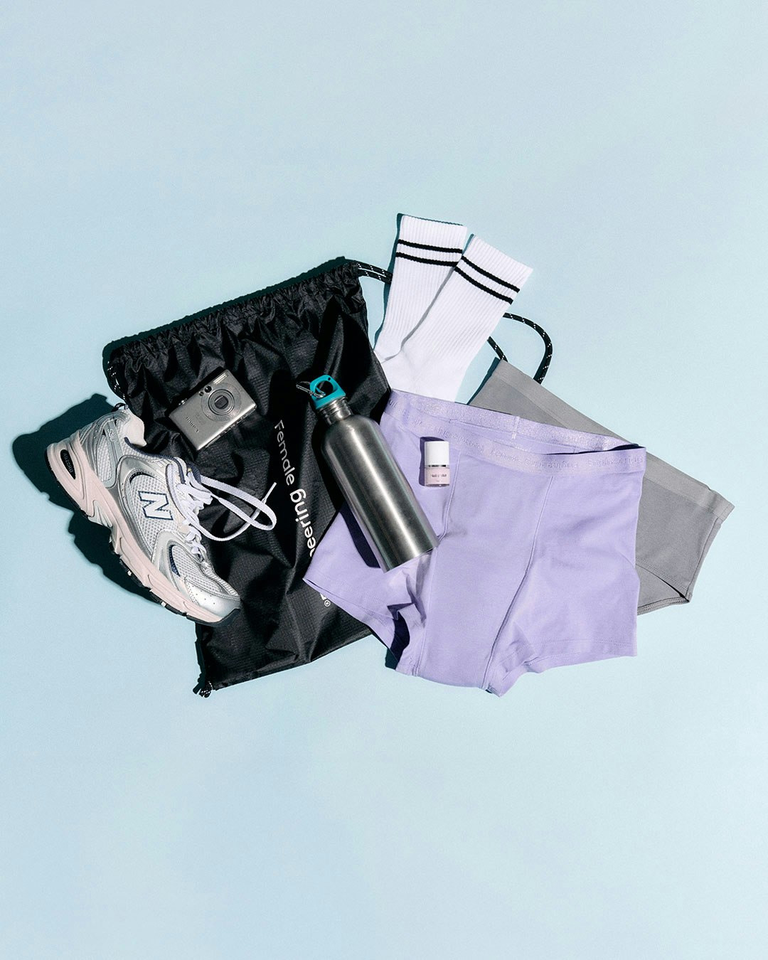 A collection of perid panties, trainers, a water bottle, and a drawstring bag on a light blue background