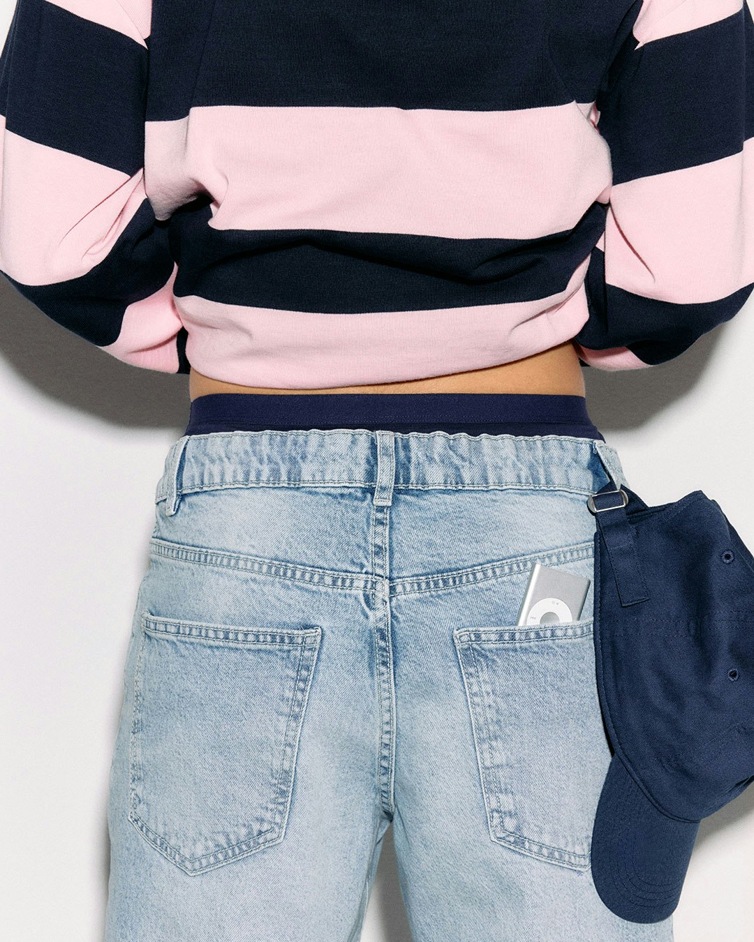 A person wearing a pink and navy striped top and light blue jeans, with a navy cap tucked in.