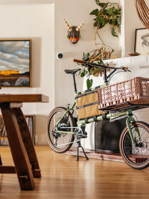 Custom green MONoPOLE cargo bike with a pink crate, displayed in a sunny living room with Albuquerque-style decor.