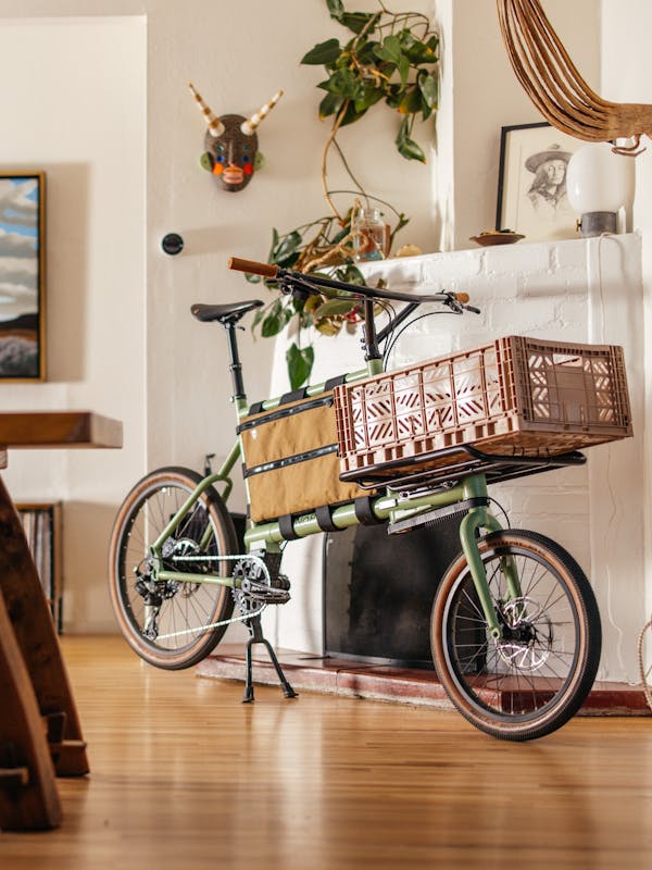 Custom green MONoPOLE cargo bike with a pink crate, displayed in a sunny living room with Albuquerque-style decor.