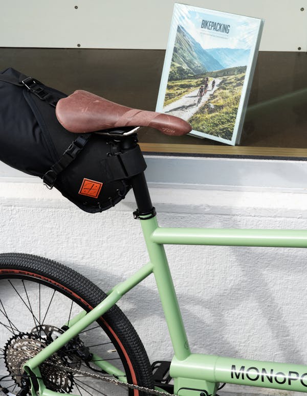 MONoPOLE Green Cargo Bike (side view), and Bikepacking Book on Store Window.