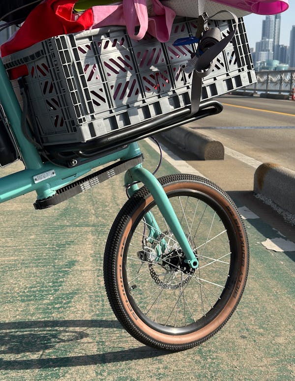 Detail of the custom MONoPOLE cargo bike, with a front platform rack, grey crate, and belt drive steering, parked on a bike lane.