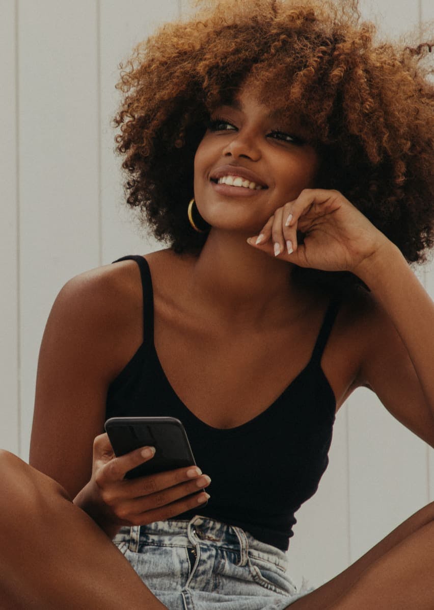Woman with fluffy hair holding her cell phone and smiling.