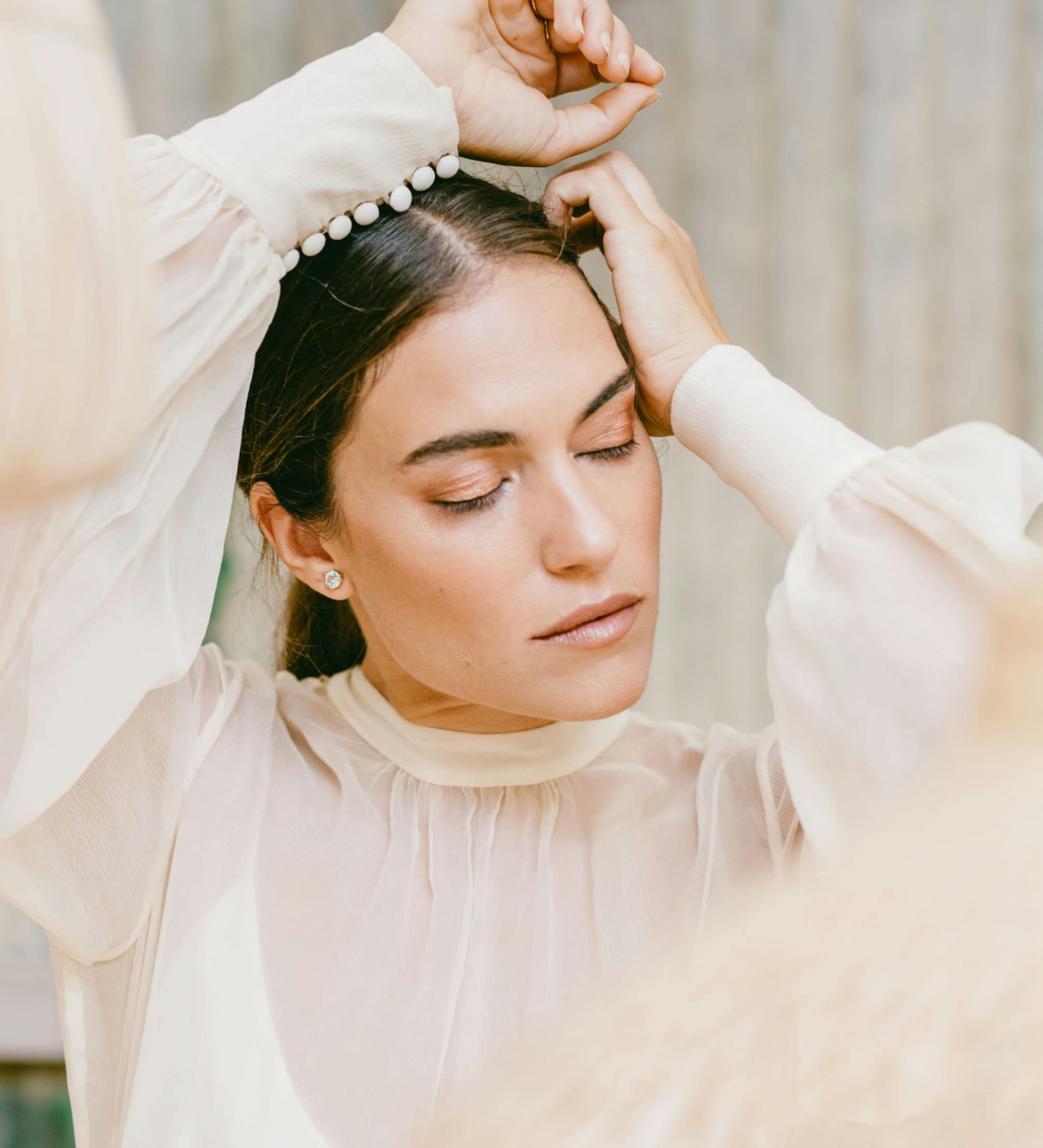 Woman in formal dress posing with her hands near her head.