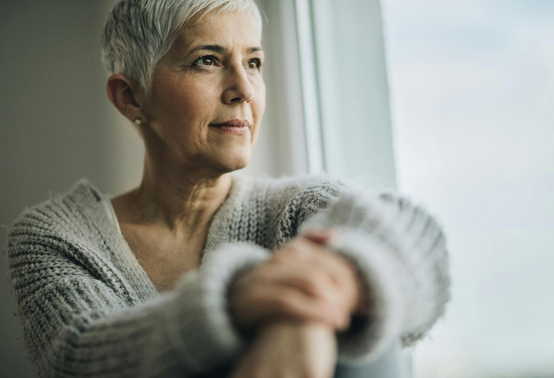 Grey haired woman looking out the window and smiling.