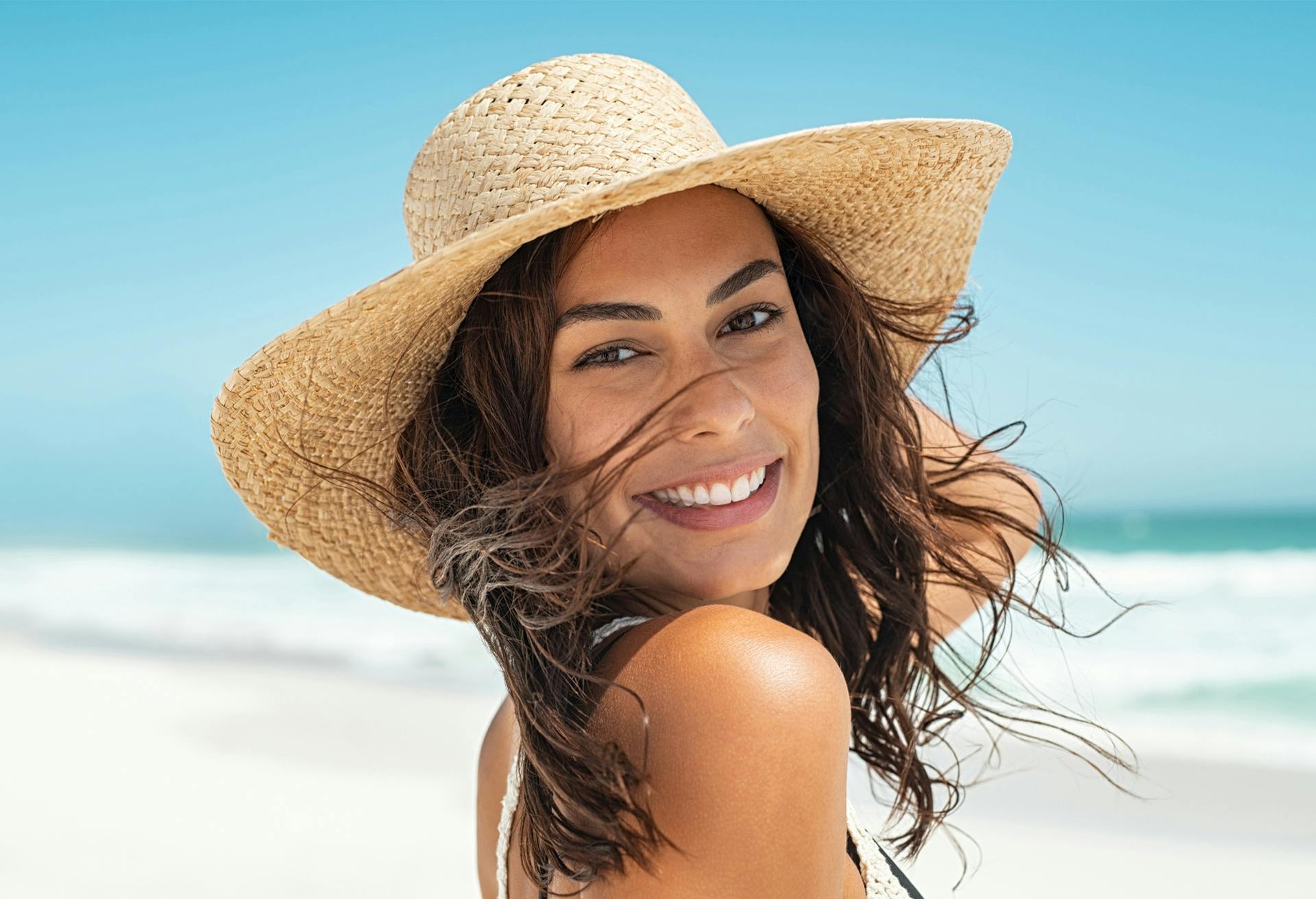 Happy brunette in a sun hat on the beach