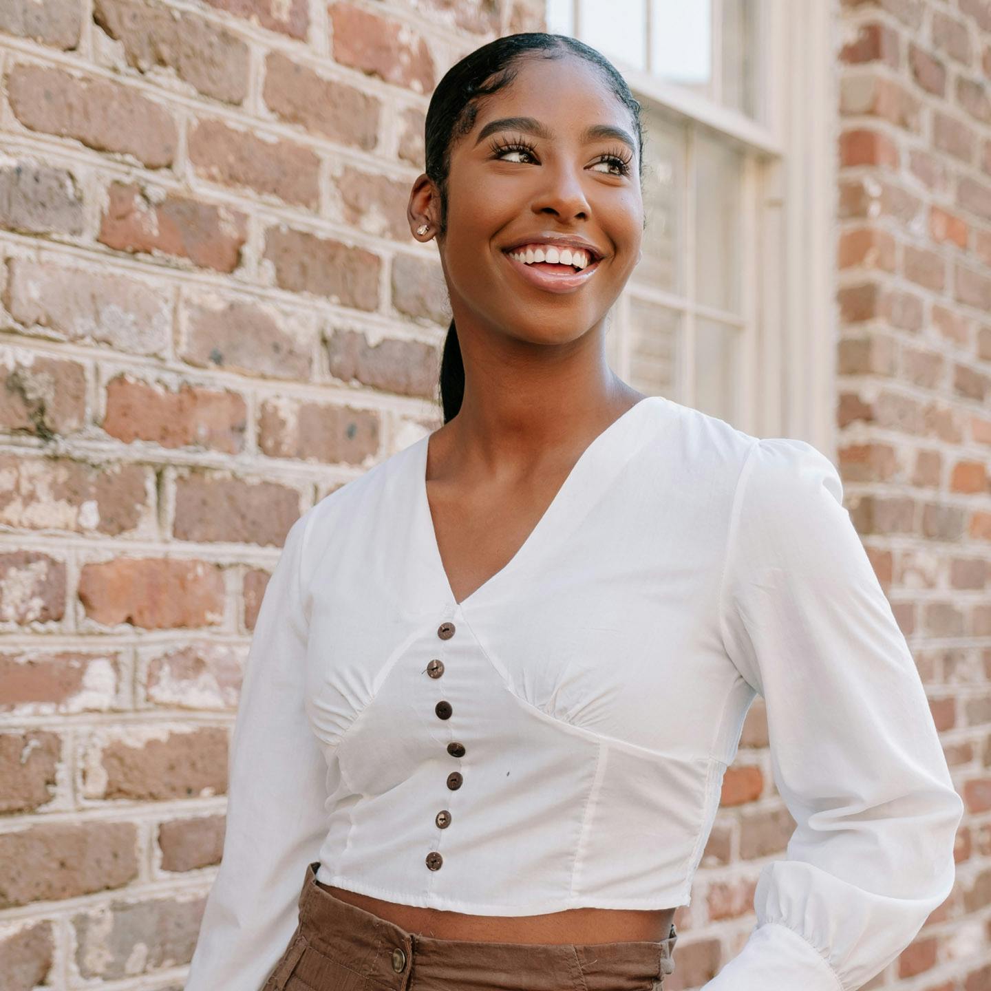 Woman smiling standing in front of a brick wall