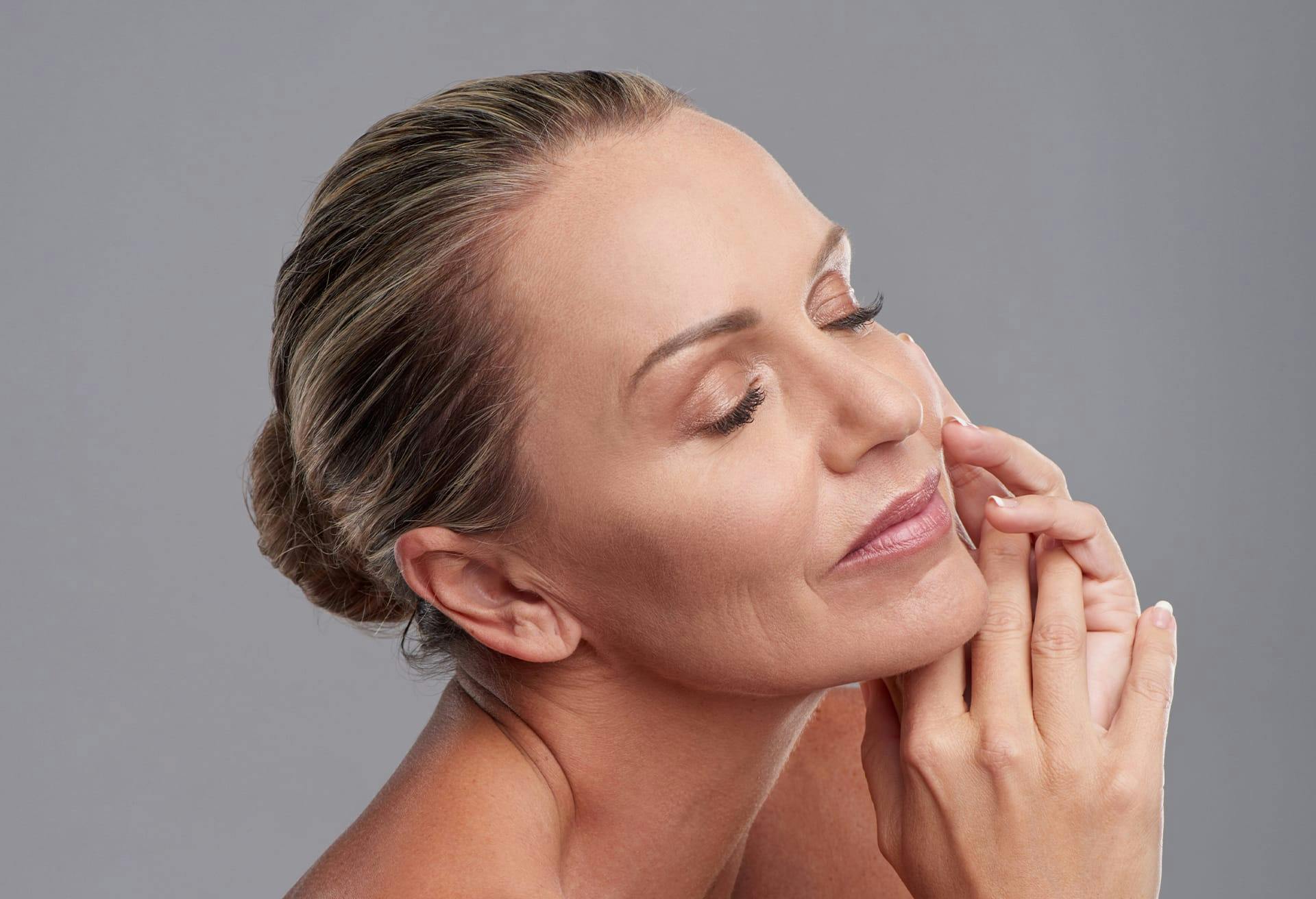 Middle aged woman facing sideways with her eyes closed, hands near her face