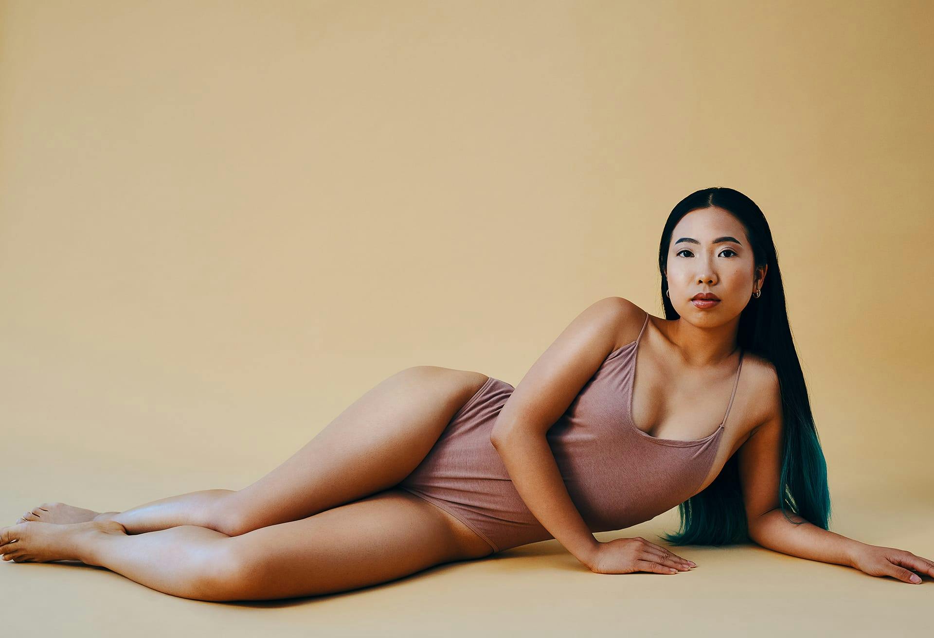 Woman laying down wearing a nudish pink bodysuit